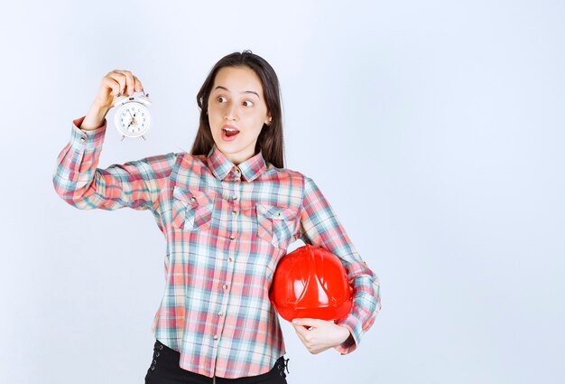 Una mujer joven que sostiene un casco y un reloj de alarma.