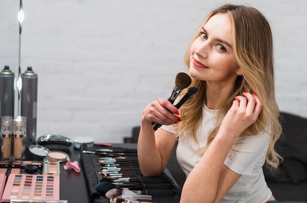 Mujer joven que sostiene los cepillos del maquillaje que se sientan en estudio