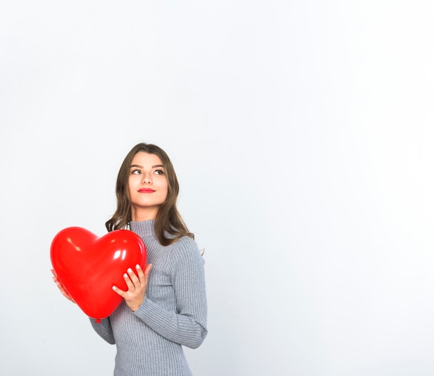 Mujer joven que sostiene el globo rojo del corazón en manos