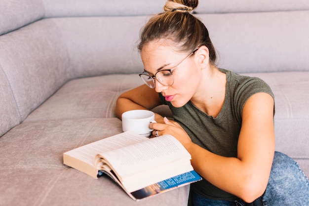 Mujer joven que sostiene el libro de lectura de la taza de café