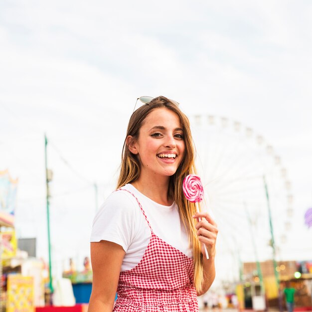 Mujer joven que sostiene la piruleta grande en el parque de atracciones