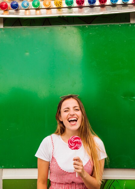 Mujer joven que sostiene la piruleta roja en su mano que ríe