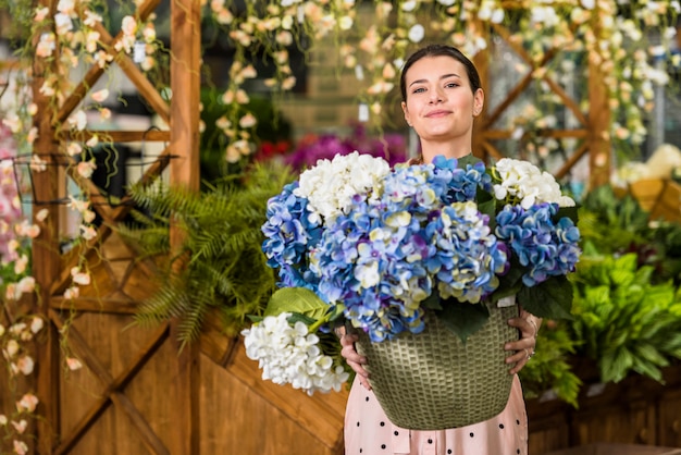 Mujer joven que sostiene el pote con las flores en casa verde