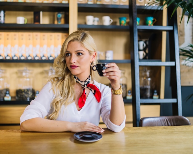 Foto gratuita mujer joven que sostiene la taza de café que mira lejos en el café