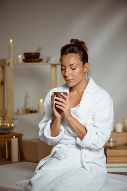 Foto gratuita mujer joven que sostiene la taza de té que se relaja en salón del balneario.