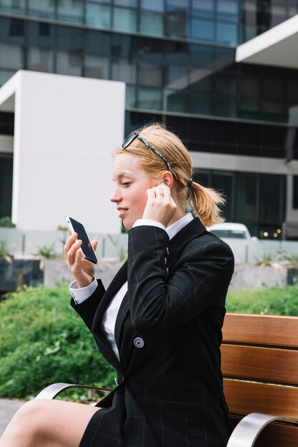 Mujer joven que sostiene el teléfono celular en la mano hablando por bluetooth inalámbrico