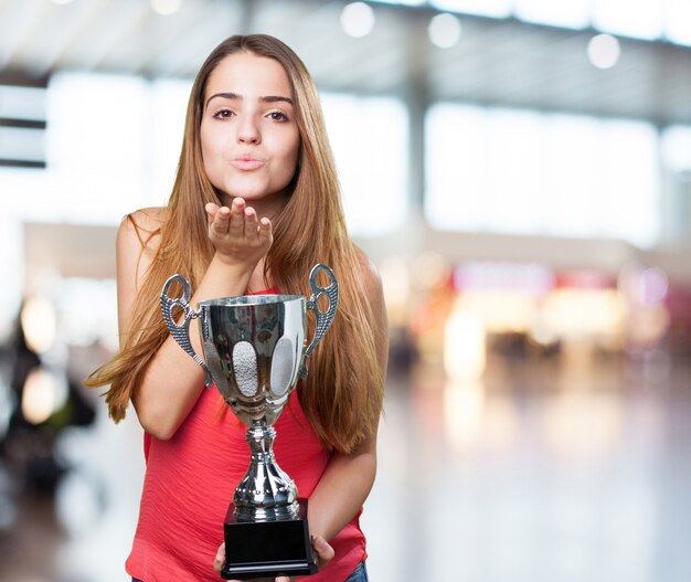 mujer joven que sostiene un trofeo y envía un beso en un backg blanco