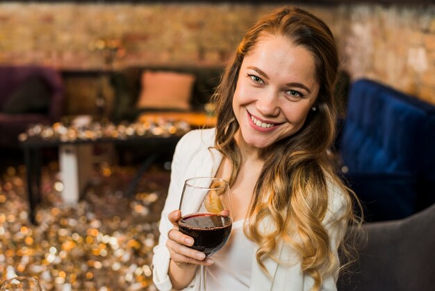 Mujer joven que sostiene un vidrio de vino rojo en barra