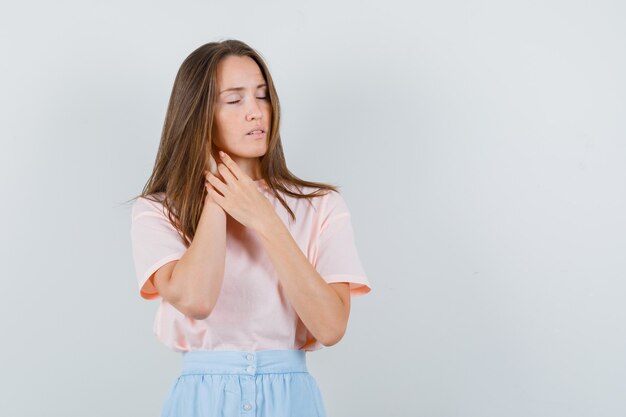 Mujer joven que sufre de dolor de cuello en camiseta, falda y con aspecto cansado. vista frontal.