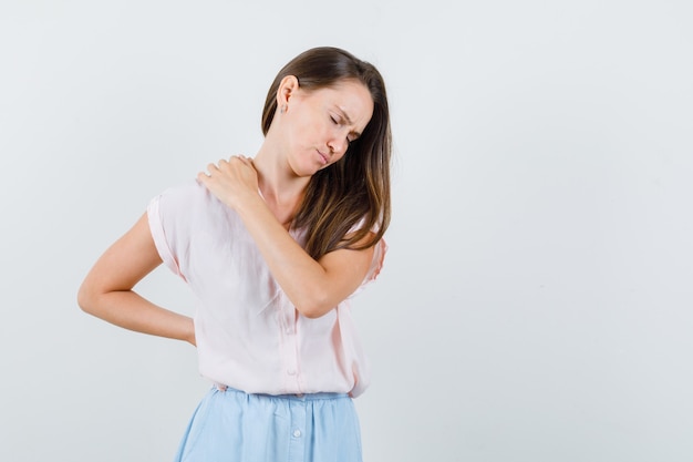 Mujer joven que sufre de dolor de espalda en camiseta, falda y aspecto cansado, vista frontal.