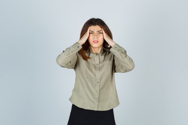 Mujer joven que sufre de un fuerte dolor de cabeza en camisa y parece molesto