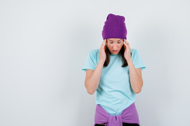 Foto gratuita mujer joven que sufre de migraña en camiseta, gorro y mirando angustiado, vista frontal.