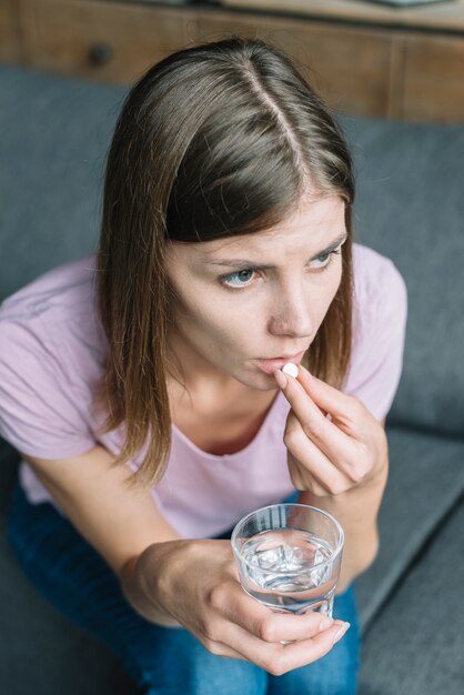 Mujer joven que tiene fiebre tomando medicina