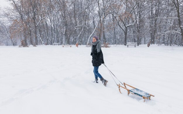 Mujer joven que tira del trineo de madera vacío en paisaje de la nieve en el bosque