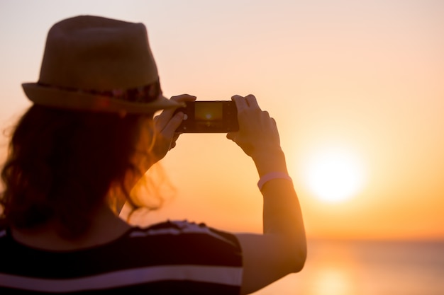 Mujer joven que toma la foto de la puesta del sol del mar