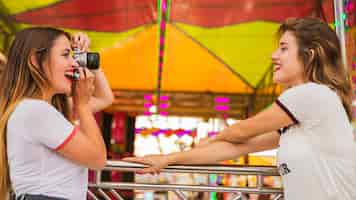 Foto gratuita mujer joven que toma la foto de su amiga sonriente en el parque de atracciones