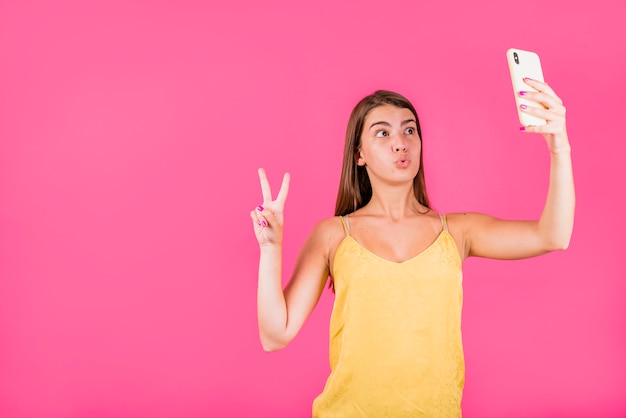 Mujer joven que toma el selfie en fondo rosado