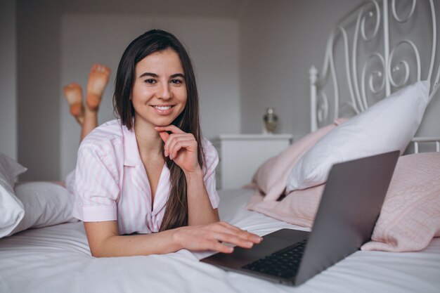 Mujer joven que trabaja en la computadora en la cama