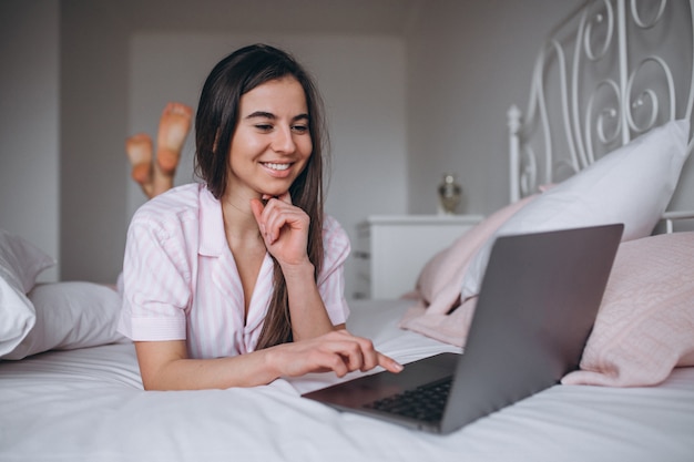 Mujer joven que trabaja en la computadora en la cama