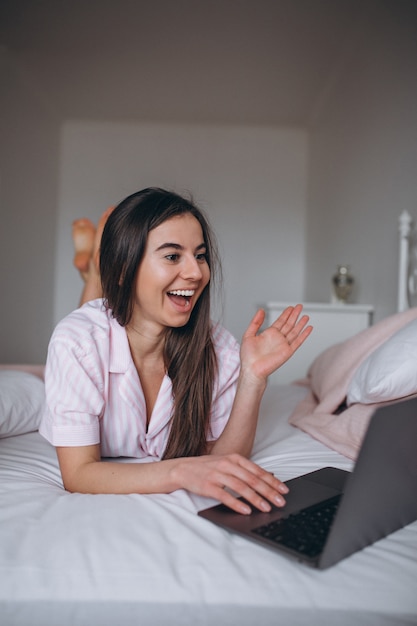 Mujer joven que trabaja en la computadora en la cama