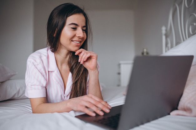 Mujer joven que trabaja en la computadora en la cama