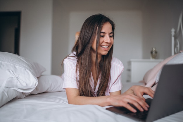 Mujer joven que trabaja en la computadora en la cama