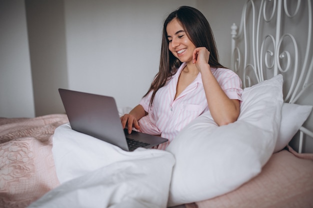 Mujer joven que trabaja en la computadora en la cama