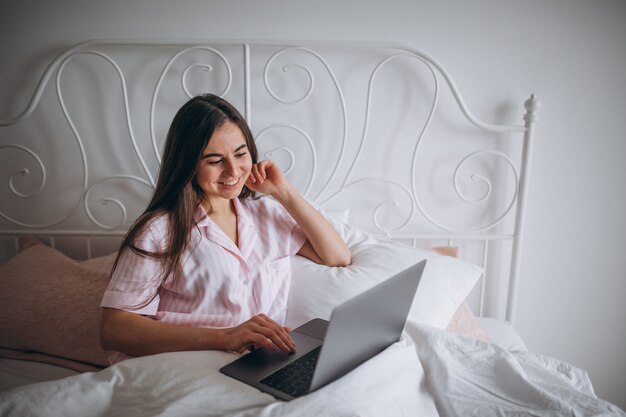 Mujer joven que trabaja en la computadora en la cama