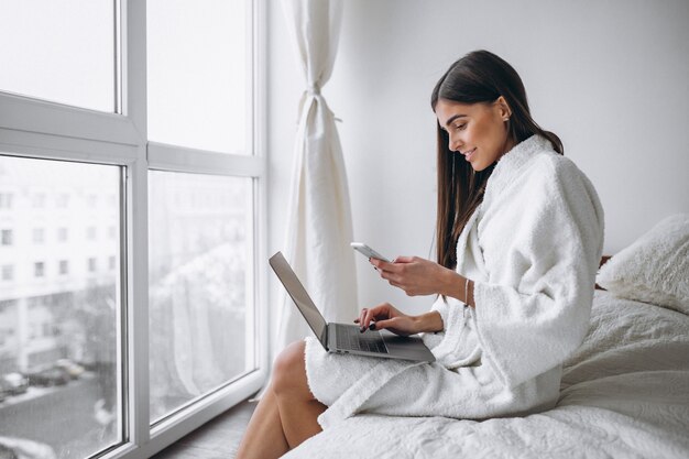 Mujer joven que trabaja en la computadora en la cama