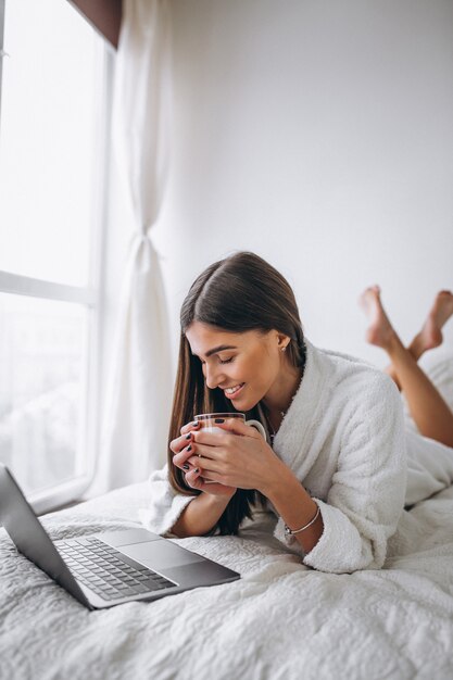 Mujer joven que trabaja en la computadora en la cama