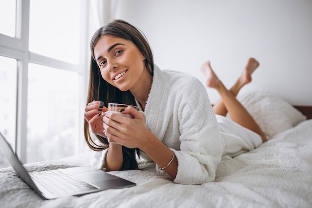 Mujer joven que trabaja en la computadora en la cama