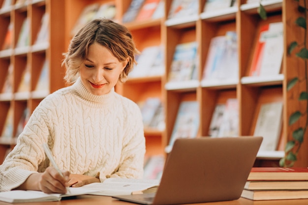 Foto gratuita mujer joven que trabaja en la computadora portátil en una biblioteca