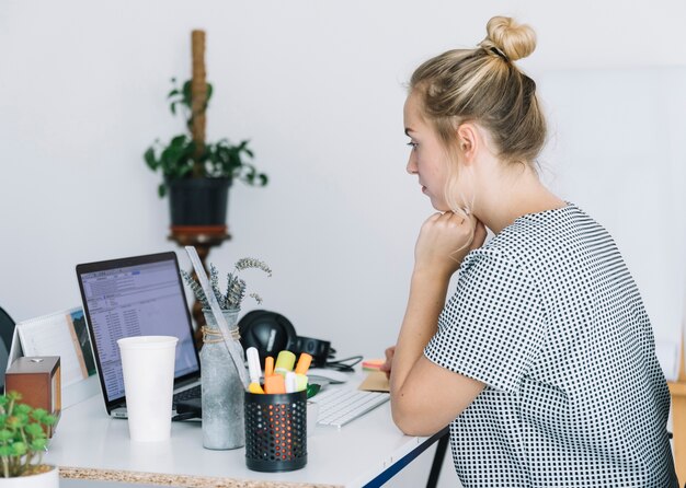 Mujer joven que trabaja en la computadora portátil en el lugar de trabajo