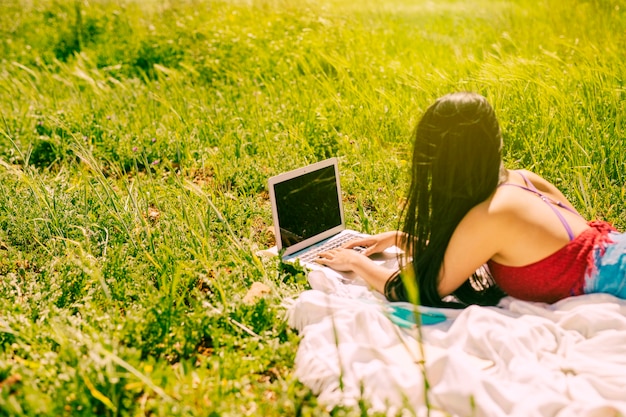 Mujer joven que trabaja en la computadora portátil en prado