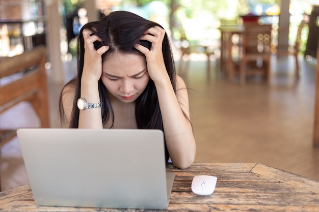 Mujer joven que trabaja en la computadora portátil que tiene un dolor de cabeza.