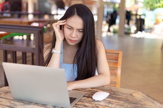 Mujer joven que trabaja en la computadora portátil que tiene un dolor de cabeza.