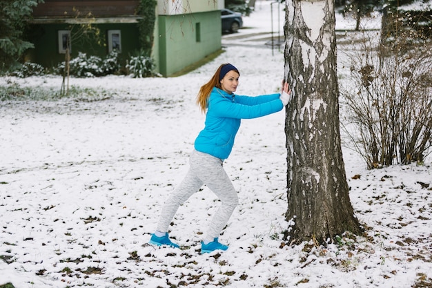 Foto gratuita mujer joven que trabaja fuera del árbol en el paisaje nevado