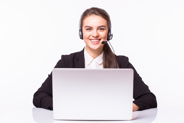 Mujer joven que trabaja en la oficina con ordenador portátil y auriculares en pared blanca, servicio al cliente y centro de llamadas.