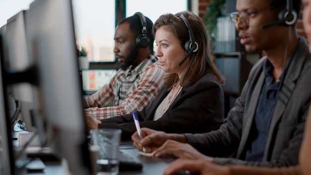 Mujer joven que usa auriculares de audio y computadora en el trabajo del centro de llamadas, ofreciendo asistencia de línea de ayuda a las personas. Consultora femenina hablando con clientes en el servicio de atención al cliente, ayudando con telemarketing.