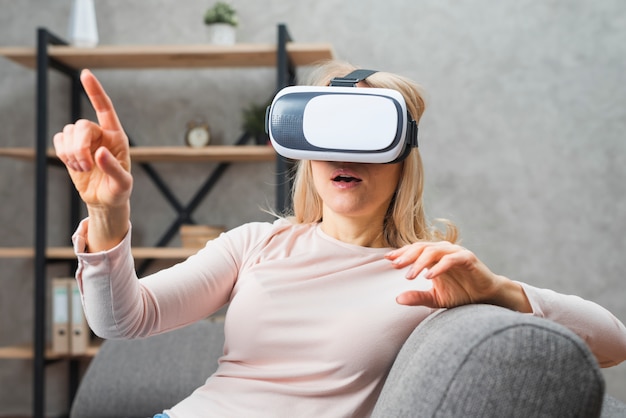 Mujer joven que usa un casco de realidad virtual apuntando con su dedo a algo