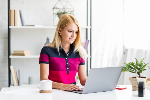 Mujer joven que usa la computadora portátil sobre el escritorio