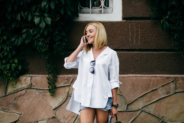 Mujer joven que usa la computadora portátil y el teléfono elegante. Muchacha hermosa del estudiante que trabaja en la computadora portátil al aire libre