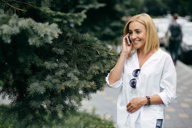 Mujer joven que usa la computadora portátil y el teléfono elegante. Muchacha hermosa del estudiante que trabaja en la computadora portátil al aire libre