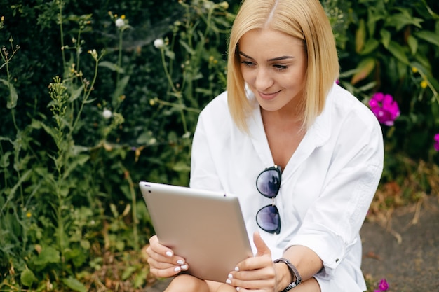 Mujer joven que usa la computadora portátil y el teléfono elegante. Muchacha hermosa del estudiante que trabaja en la computadora portátil al aire libre