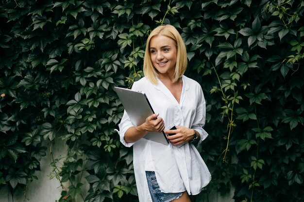 Mujer joven que usa la computadora portátil y el teléfono elegante. Muchacha hermosa del estudiante que trabaja en la computadora portátil al aire libre