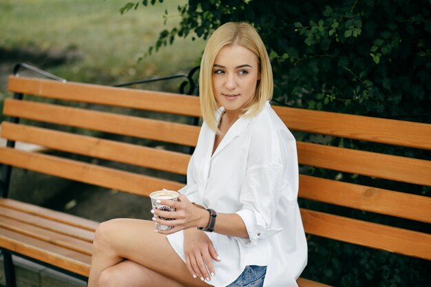 Mujer joven que usa la computadora portátil y el teléfono elegante. Muchacha hermosa del estudiante que trabaja en la computadora portátil al aire libre