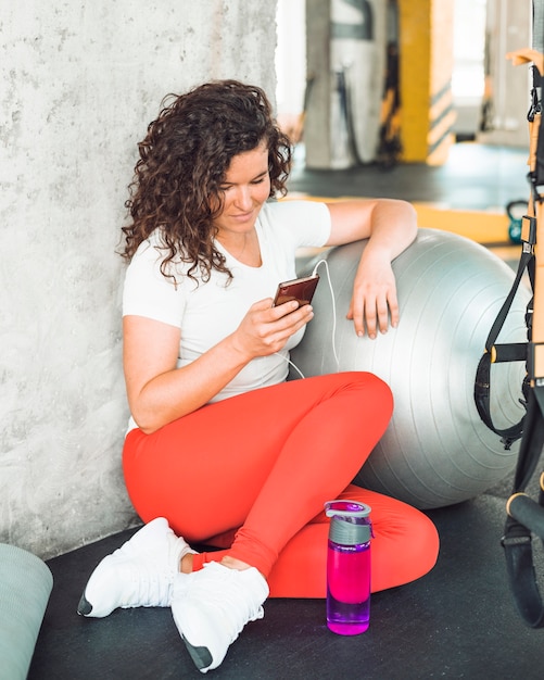 Mujer joven que usa smartphone después de entrenamiento en gimnasio