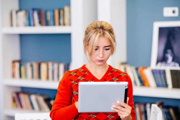 Mujer joven que usa la tableta en biblioteca