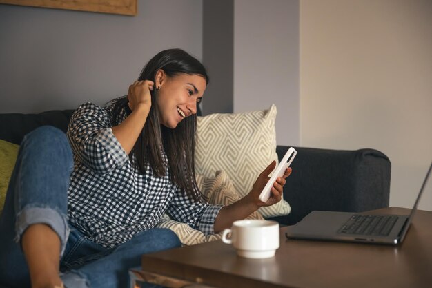 Una mujer joven que usa un teléfono inteligente y una computadora portátil en casa