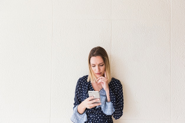 Foto gratuita mujer joven que usa el teléfono móvil delante de la pared